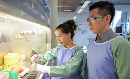 Two scientists in lab coats and goggles working in a lab.